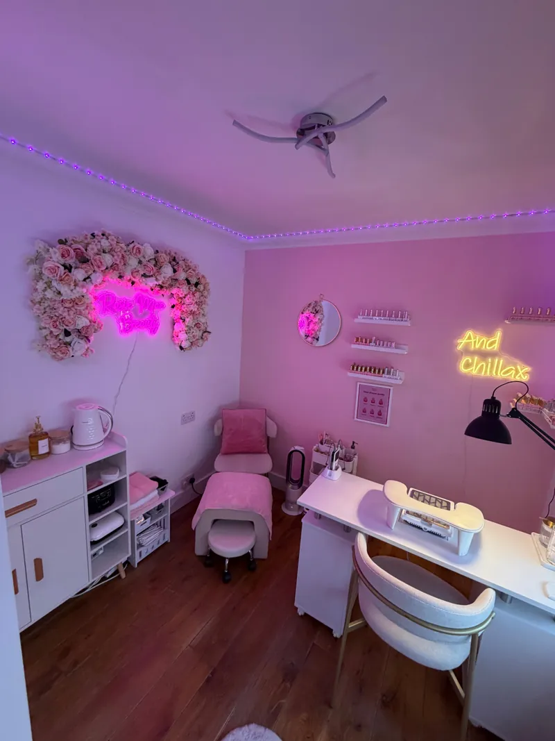 Rosie's nail room: pink walls, her neon sign in a wall of flowers, a white nail desk and a second neon sign that reads And Chillax